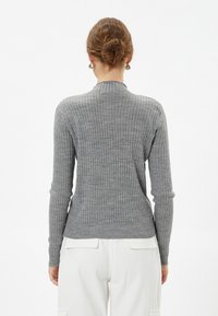 Maglione grigio a maniche lunghe con colletto alto e silhouette aderente. Presenta un tessuto lavorato e orli e polsini a coste.