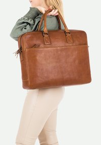 Borsa per laptop in pelle marrone con due manici superiori, chiusura con zip e tasca esterna. Texture liscia con dettagli cuciti e hardware resistente.