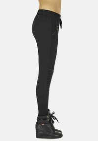 Czarne dresowe spodnie z elastycznym pasem na sznurek, zamykanymi kieszeniami na zamek oraz prążkowanymi akcentami po bokach, w zestawieniu z teksturowanymi sneakersami za kostkę.