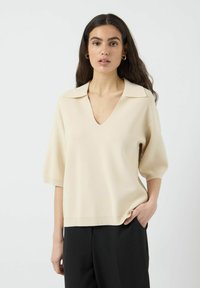 Beige neule, jossa on V-pääntie, lyhyet dolman-hihat, ribbaatut hihansuut ja rento malli, valmistettu pehmeästä, teksturoidusta neulekankaasta.