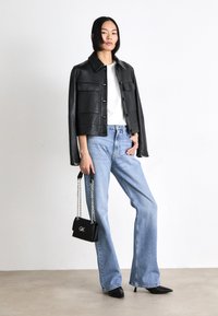 Chaqueta de cuero negra con bolsillos frontales, camiseta blanca, vaqueros de pierna ancha en azul claro, zapatos de tacón negro con punta y sosteniendo un pequeño bolso negro.