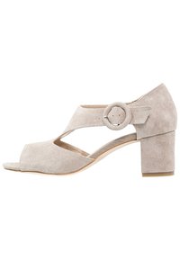 Sandalo con tacco in suede beige caratterizzato da un dettaglio accentato rotondo, design a punta scoperta e un robusto tacco a blocco. Parte superiore testurizzata con lati intagliati.