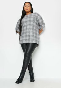 Blusa oversize a quadri grigia con maniche arrotolate e dettagli con bottoni, abbinata a leggings in finta pelle nera attillati e stivaletti.