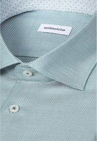 Gros plan d'une chemise texturée bleu clair avec des boutons blancs et un col intérieur à motifs, étiquetée "seidensticker."