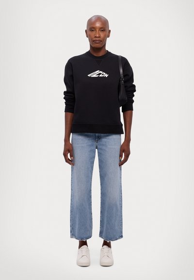 Black sweatshirt with a white logo, light blue wide-leg jeans with raw hem, and white sneakers. Simple, casual outfit on a model.