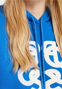 Blue hoodie with white graphic lettering, featuring a drawstring closure with blue tips. The fabric appears smooth and soft.