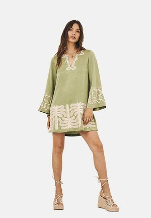 Vestido verde de túnica con mangas acampanadas de tres cuartos, bordado decorativo en blanco en el escote y el dobladillo, con un patrón de hojas de palma.