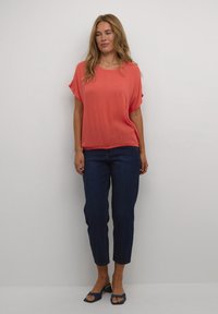 Haut corail à manches courtes associé à un jean cropped bleu marine et des sandales navy. Le haut a une coupe décontractée et une texture lisse.