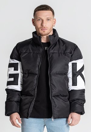 Chaqueta de plumas en blanco y negro con un alto cuello, cierre de cremallera y grandes acentos de logo en las mangas. Presenta una textura acolchada y una silueta inflada.