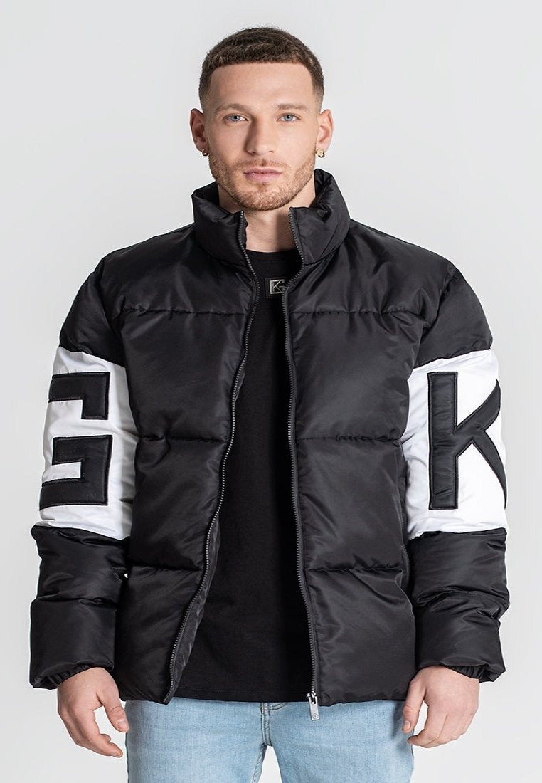 Chaqueta de plumas en blanco y negro con un alto cuello, cierre de cremallera y grandes acentos de logo en las mangas. Presenta una textura acolchada y una silueta inflada.