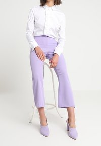 White blouse with ruffled front, paired with light purple tailored pants. Soft texture, flared hem, and matching purple heels.
