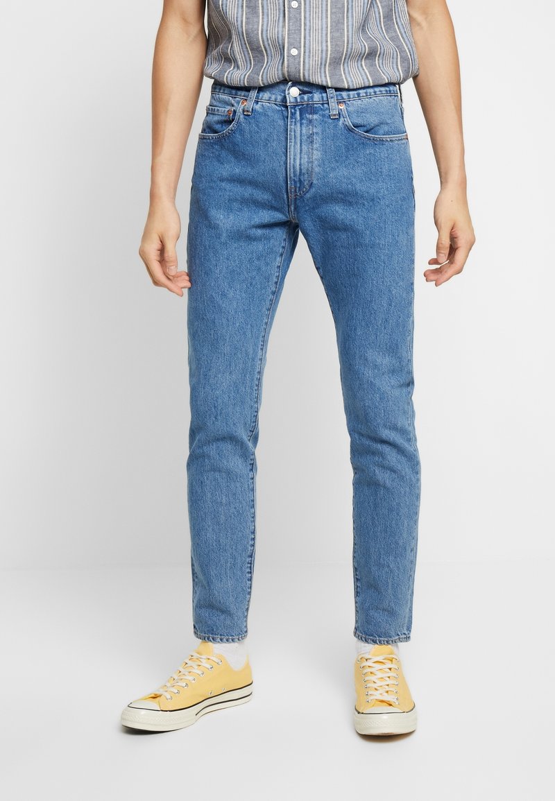 Ljusblå denimjeans med slim fit, fem fickor och synlig sömnad. Matchas med gula låga sneakers.