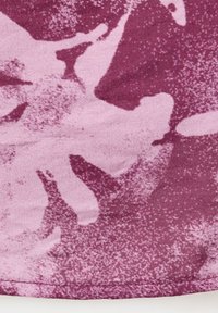 Nærbillede af lilla stof med lyserødt abstrakt blomsterprint og synligt syning langs nederste kant.