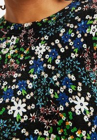 Czarny materiał z gęstym wzorem kwiatowym w kolorach niebieskim, białym i zielonym. Wzór zawiera różne kształty kwiatów oraz żywe zielone liście.