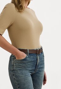 Top beige aderente a maniche corte, abbinato a jeans blu a vita alta e una cintura marrone. Texture liscia e design semplice.