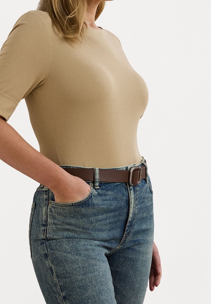 Top beige aderente a maniche corte, abbinato a jeans blu a vita alta e una cintura marrone. Texture liscia e design semplice.
