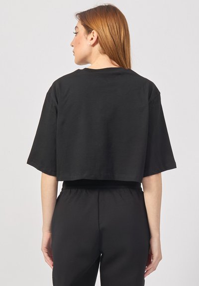 Maglietta nera in cotone tagliata, con maniche corte, orlo dritto e scollatura pulita, mostrata da dietro.