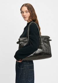 Schwarze Lederhandtasche mit einer strukturierten Oberfläche, ausgestattet mit zwei Griffen oben und einem Schnallendetail. Das Design ist strukturiert und geräumig.