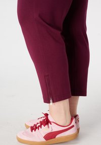 Pantalon capri bordeaux avec fermeture éclair latérale, associé à des baskets en daim rose avec des accents rouges et une semelle en caoutchouc gomme.