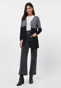Gray and black color-blocked cardigan with open front, ribbed cuffs, two front pockets, worn over a white shirt and black high-waisted jeans.