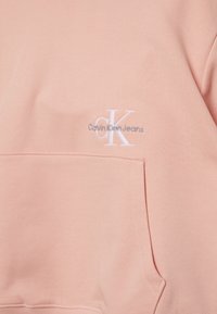 Světle růžová mikina s přední kapsou a bílým vyšitým logem "CK Calvin Klein Jeans" na hrudi.