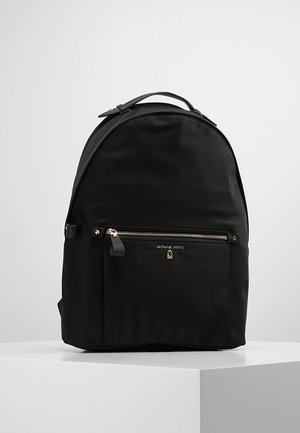 Czarny plecak Michael Kors z przednią kieszenią na suwak, górnym uchwytem i regulowanymi paskami na ramiona, wystawiony na białym piedestale.