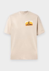 Beige bomull T-skjorte med et grafisk trykk av en figur i en yoga-pose mot en fargerik solnedgangsbakgrunn. Korte ermer, rund hals.