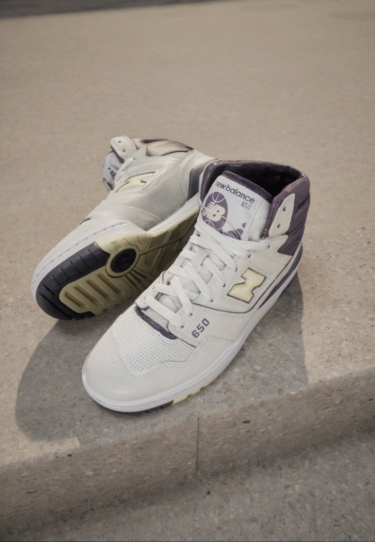 Wysokie sneakersy ze białej skóry z purpurowymi akcentami, perforowaną fakturą, gumową podeszwą i wyraźnym logo "N" po boku.
