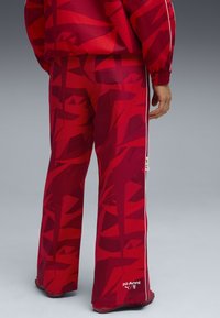 Rode sportieve broek met abstracte patronen, voorzien van witte zijstrepen en een logo-detail bij de zoom. Textuurstof.