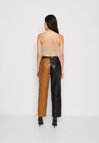 Bruna och svarta läderbyxor med rak passform, hög midja och sömdetaljer. Bärs med en beige crop top och svarta högklackade skor.