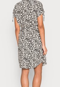 Abito floreale in bianco e nero con maniche corte e tasche laterali. Presenta una vestibilità ampia e una vita arricciata per dare forma.