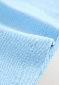 Vaaleansininen teksturoidu kangas, jossa on waffle-kuviointi, taitettuna näyttämään ompelun yksityiskohtia ja pehmeää kudottua pintaa.