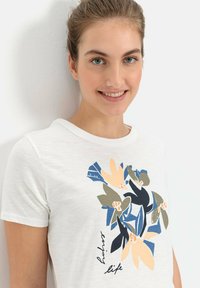 Witte katoenen t-shirt met een bloemenprint in blauw, groen en perzik, met de tekst "holus life" op het ontwerp. Ronde halslijn.