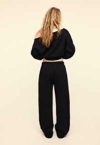 Schwarzer kurz geschnittener Sweatshirt mit weiten Ärmeln und elastischem Saum, kombiniert mit lockeren schwarzen Sweatpants mit glatter Textur.