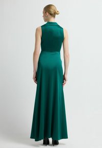 Długa zielona satynowa sukienka z kołnierzykiem, bez rękawów i z rozłożystą spódnicą. Tył ma dopasowany gorset i gładką fakturę.