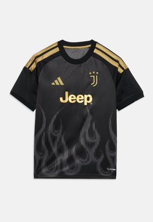 Camiseta de fútbol negra con franjas doradas de Adidas en los hombros, logo dorado de Jeep, emblema de la Juventus y un sutil patrón de llamas en la parte inferior.