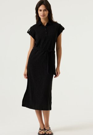 Robe noire jusqu'aux genoux avec un col à revers, des manches courtes retroussées et une ceinture en tissu. Fabriquée en matériau texturé avec une coupe décontractée.