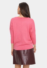 Pull en maille rose à manches trois-quarts, avec une coupe décontractée et une couture à l'arrière. Associé à une jupe en cuir synthétique bordeaux.
