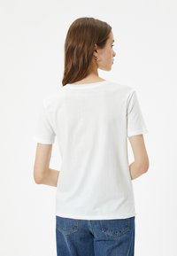 T-shirt en coton blanc à manches courtes et col rond, présenté de dos, associé à un jean en denim bleu.