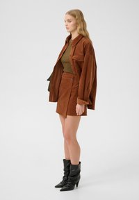 Set di giacca e gonna in corduroy ruggine con un top fitted color oliva, abbinato a stivali alla caviglia neri e slouchy con punta affilata.