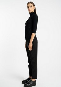 Czarny dopasowany top z długim rękawem i wysokim kołnierzem, zestawiony z dopasowanymi czarnymi spodniami i masywnymi czarnymi butami. Prosty, elegancki design.