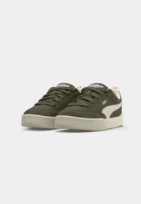 Olive green suede sneakers with white accents, textured upper, and flat rubber sole, featuring a lace-up design and logo on the tongue.