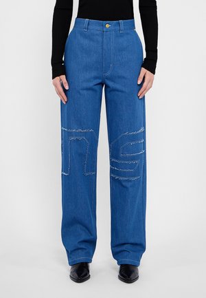 Bredde ben, blå denimbukser med høy midje. Har kontraststing og en stor, sydd "NS" detalj på hvert ben. Klassisk knappelukking.