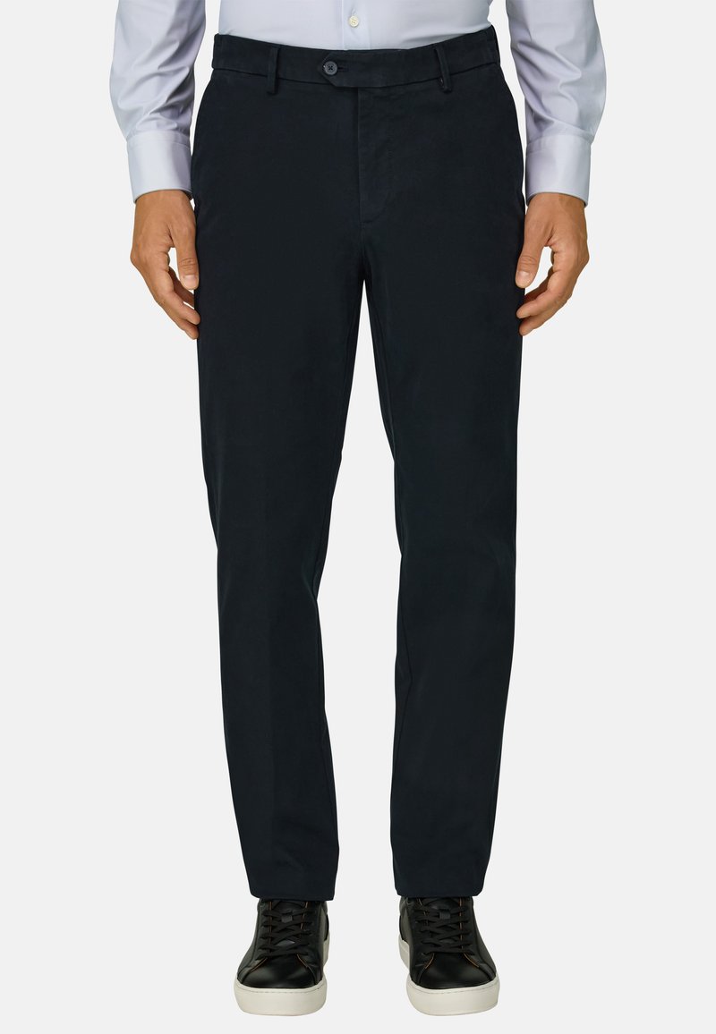 Homme portant un pantalon droit noir, une chemise bleue claire boutonnée et des baskets noires à semelles blanches, debout, bras détendus.
