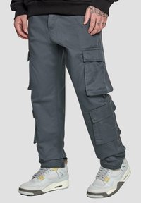 Grå cargo bukser med flere sidelommer, lavet af slidstærkt stof, med afslappet pasform og subtil glans. Sammen med lysegrå sneakers.