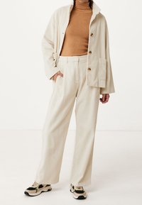 Beige corduroy jacket with large buttons, paired with matching high-waisted corduroy pants. Brown ribbed turtleneck beneath. Chunky sneakers.
