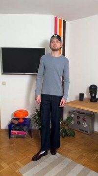 Világoskék hosszú ujjú bordázott póló hajtókás ujjakkal, sötét széles szárú farmernadrág és sötét mokaszinok. Narancssárga lámpa és zöld növények a háttérben.