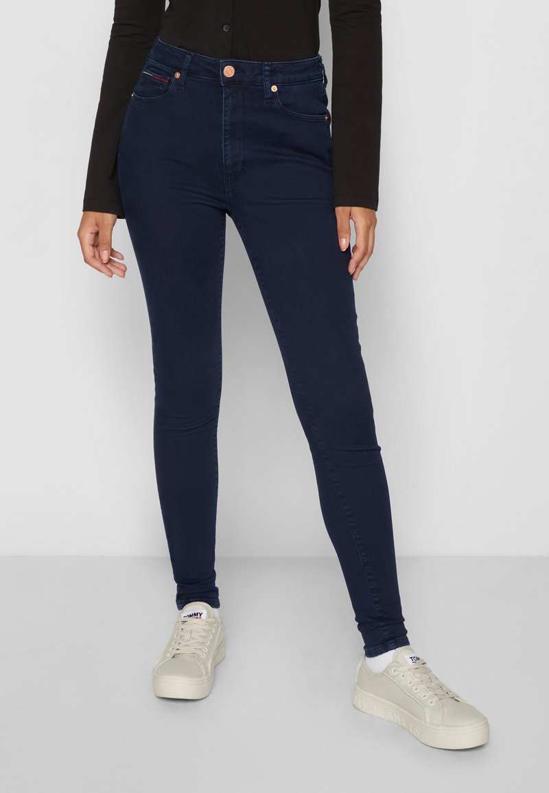 Mørkeblå høytaljede skinny jeans laget av denim, med kobberknapper og nitter, frontlommer og en glatt tekstur.