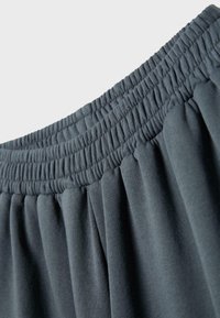 Ciemnoszara elastyczna gumka w pasie z marszczonym materiałem, ukazująca szczegółowe przeszycia i fakturę miękkiego materiału.