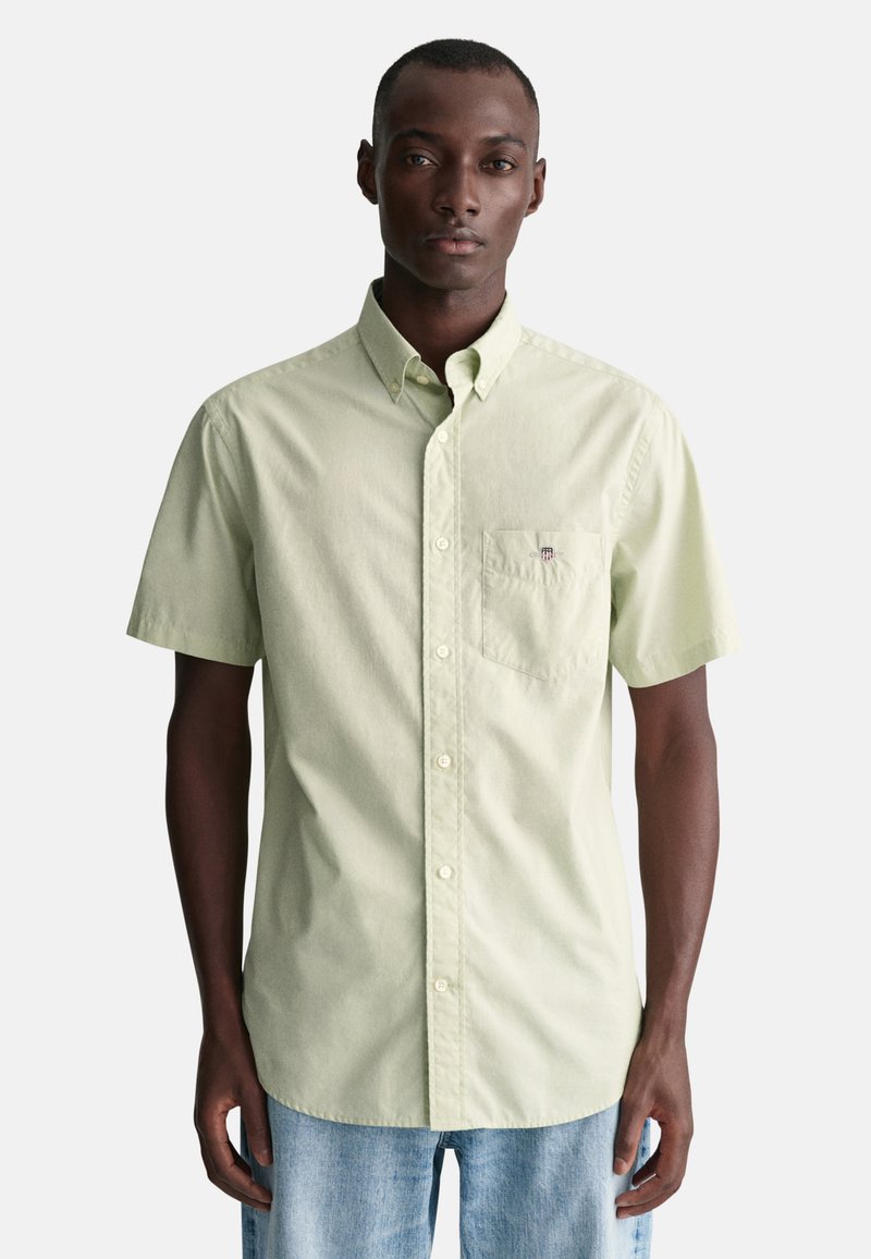Camisa de botones de manga corta en verde claro, con un bolsillo en el pecho y el logo de la marca, hecha de algodón con una textura suave.
